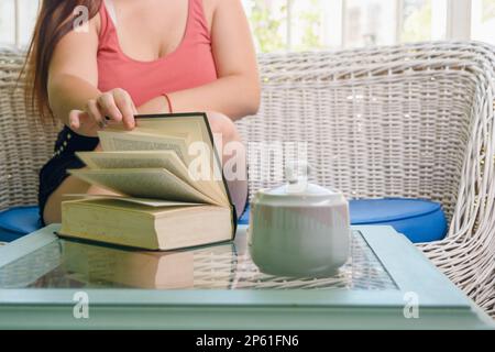young unrecognizable woman, sitting at home, flipping through the pages of a book on the table, lifestyle concept, copy space. Stock Photo