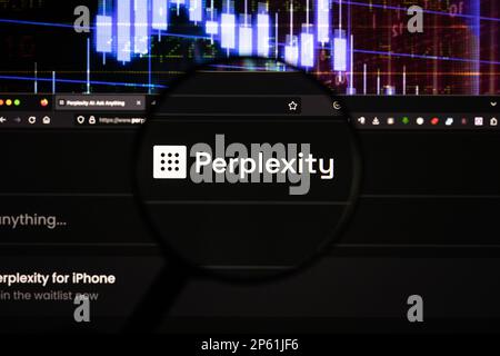 Perplexity chatbot company logo on a website with blurry stock market developments in the background, seen on a screen through a magnifying glass Stock Photo