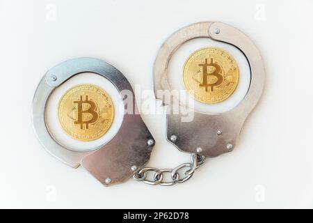 prison for using payments in cryptocurrency. Handcuffs and a golden bitcoin on a white background table. Stock Photo