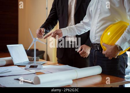 Team of architect and engineer having a discussion while working with wind turbine models and blueprints. Creative businesspeople working on a renewab Stock Photo