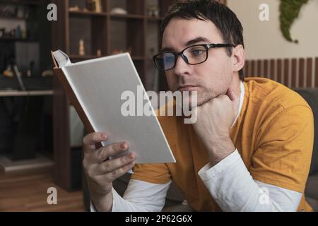 Adult handsome smiling man in glasses reading book while sitting Stock Photo