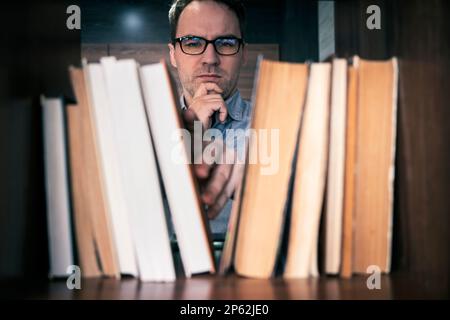 male hand choosing and picking book in public library, education research and self learning in university life concepts Stock Photo