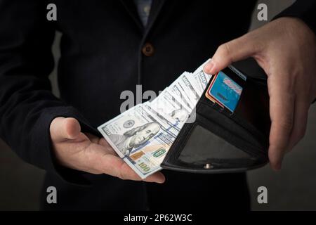Man hands with leather wallet. Right hand is pulling American money - US Dollars. getting a salary, a lot of money in wallet. Stock Photo
