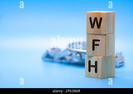 WFH text represent work from home text engraved on wooden blocks with light blue and watch background. Work from home concept. Copy space. Stock Photo