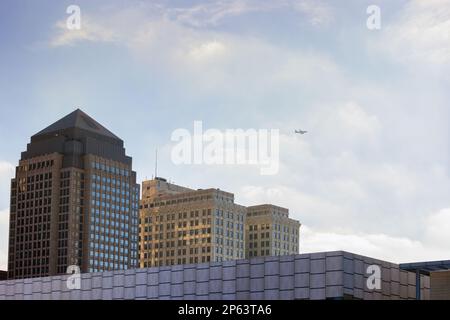 Tops of buildings under cloudy bright skies with a plane flying overhead in downtown Cleveland, Ohio. Stock Photo