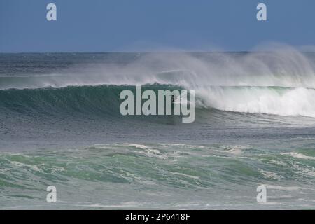 Perfect surfing waves roll into Bells Beach. A surfer tucks in beneath the crest of the wave in strong offshore winds when spray curls into the air Stock Photo
