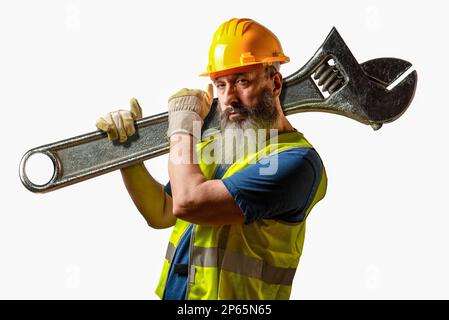 Man in helmet and yellow vest holding a giant spanner over his shoulder on white background. Stock Photo