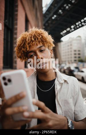 Active mixed race teenager smiling and typing message at the smartphone while walking at the city Stock Photo