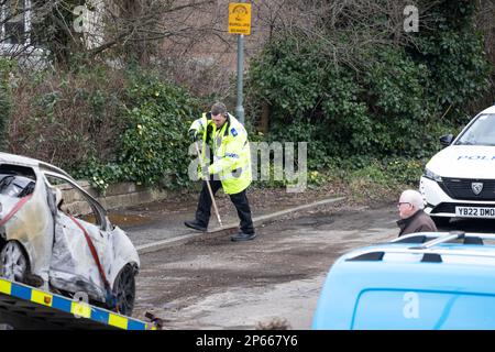 Police Community Support Officer sweeping the road of debris after the recovery of the burnt out remains of a torched  car in West Yorkshire U.K. Stock Photo