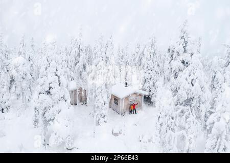 Aerial view of happy couple enjoying the winter holidays in a frozen hut in the snowy forest, Iso Syote, Northern Ostrobothnia, Lapland, Finland Stock Photo