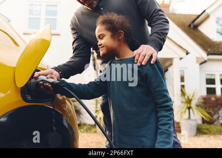 Father helping son with Down syndrome plug electric charger into car Stock Photo