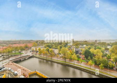 Amsterdam, Netherlands - 10 April, 2021: a river with buildings in the background and trees on both sides, taken from a high angle looking down at an overcast sky Stock Photo