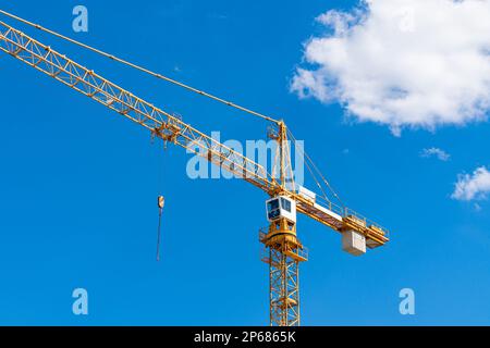 Yellow tower crane with white cab against blue sky. Light clouds float across the sky. Stock Photo