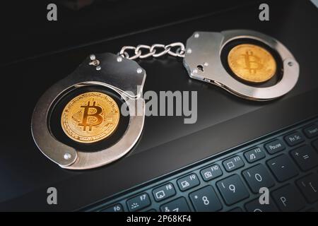 a golden bitcoin on the background of handcuffs and a black laptop keyboard. Prohibition of the sale and purchase of bitcoin and cryptocurrencies. Stock Photo