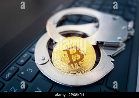 a golden bitcoin on the background of handcuffs and a black laptop keyboard. Prohibition of the sale and purchase of bitcoin and cryptocurrencies. Stock Photo