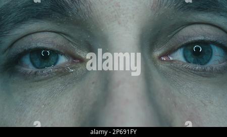 Close-up macro shot of a crying eye. Young handsome guy with natural light blue, yellow and green pigmentation on the iris. Tears flow down Stock Photo