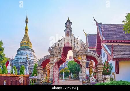 The sculptured and frescoed stucco gate with Devata deities, Nagas, Garudas, hams swans in front of historic Chedi of Wat Buppharam, Chiang Mai, Thail Stock Photo