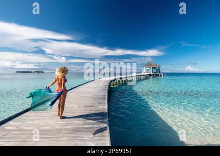 Young woman with a sarong walking on the wooden jetty of a Maldivian resort Stock Photo