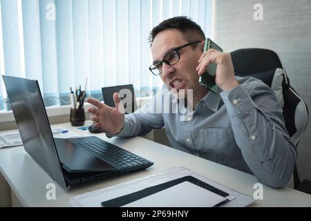 Angry businessman talking on the phone in office. aggression and stress of the boss. Emotional business communication over the phone. the evil boss is Stock Photo