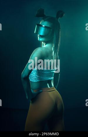 Portrait of beautiful cyber model woman posing wearing futuristic glasses on head with neon light in a virtual tech environment Stock Photo