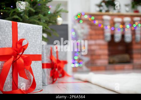 Silver gifts with red ribbons under Christmas tree and fireplace in bacground. Stock Photo