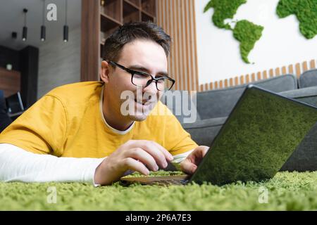 Handsome young man laying on floor at home, browsing internet smiling. Stock Photo