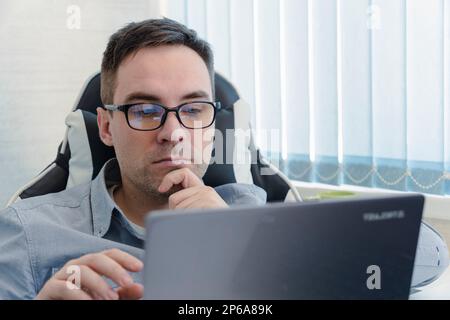startup business, software developer working on computer at modern office. a thoughtful young handsome guy writes a program in a bright white office. Stock Photo