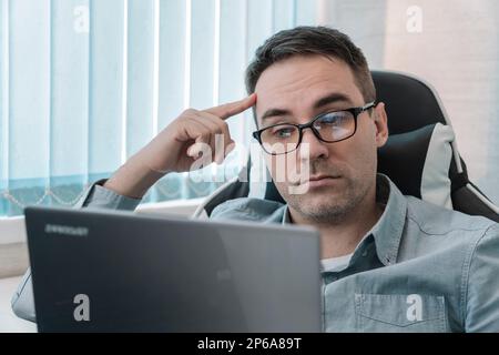 Thoughtful it developer thinking about fixing software bugs on netbook. contemplative male student watching tutorial on web site learning online via l Stock Photo