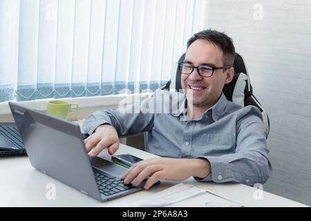 Smiling young man working on laptop in modern kitchen, checking email in morning, writing message in social network, happy male using internet, search Stock Photo