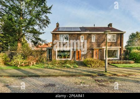 Amsterdam, Netherlands - 10 April, 2021: an old brick house with solar panels on the roof and two windows, in front of it is a garden Stock Photo