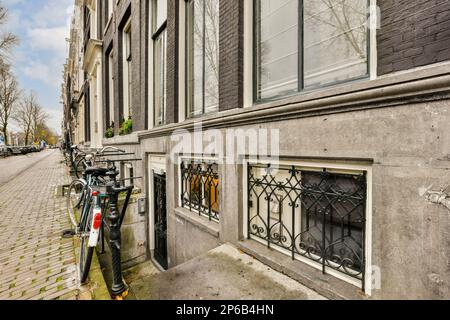 Amsterdam, Netherlands - 10 April, 2021: a bike parked on the side of a street in front of a building with many windows and balknots Stock Photo