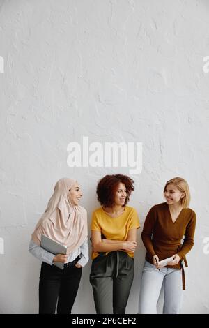 Three elegant smiling young women with different ethnicity standing over white wall background. Stock Photo