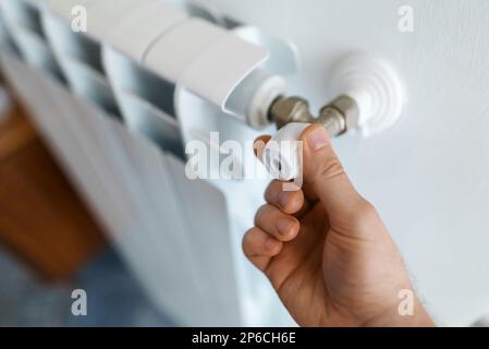 Male hand adjusting thermostat to turn on the radiator heater at home. Stock Photo