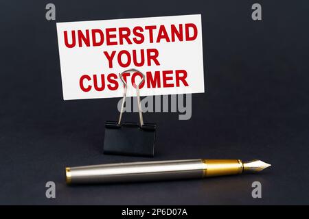 Business concept. On the black surface is a pen, an office paper clip with a business card on which is written - UNDERSTAND YOUR CUSTOMER Stock Photo