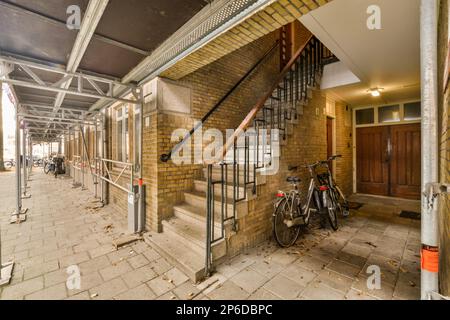 a bike parked in front of a brick building with stairs leading up to the second floor and an open door Stock Photo