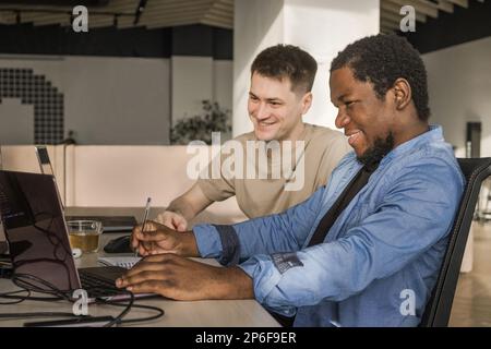 Two smiling positive programmers working in the office of a software development company. Coding technologies, site design. Successful diverse Stock Photo