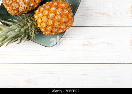 Juicy pineapples in a green plate on a white wooden background. Healthy, detox and dietary nutrition concept. Stock Photo