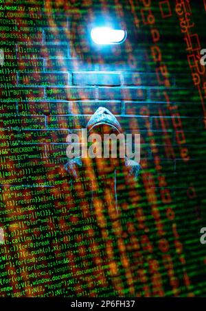 A hacker in a hoodie behind lines of code Stock Photo