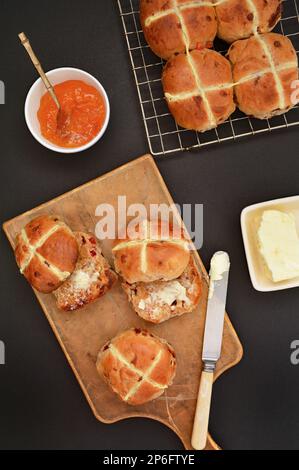 Fresh baked hot cross buns on black background in flat lay composition in vertical format.  Traditional Easter treat. Stock Photo