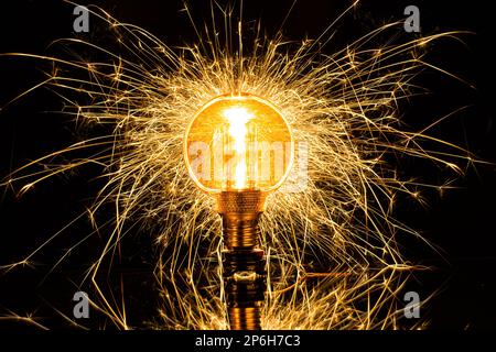 Isolated lighted up incandescent lamp with fire sparks and filament in a black background. Electricity concept. Stock Photo