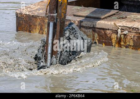 Dredging the bottom of water area, view of the bucket of the floating excavator full of mud Stock Photo