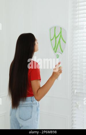 Young woman with electric fly swatter indoors. Insect killer Stock Photo