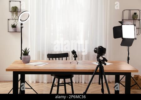 Camera and lighting equipment on tripods near table in room. Blogger workplace Stock Photo