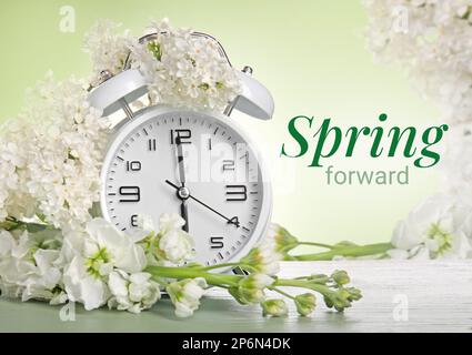 Alarm clock and white flowers on green background. Spring time Stock Photo