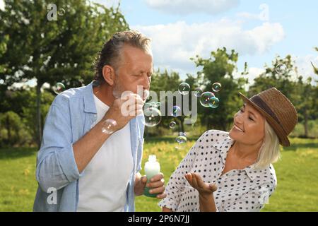 Lovely mature couple spending time together in park. Man blowing soap bubbles Stock Photo