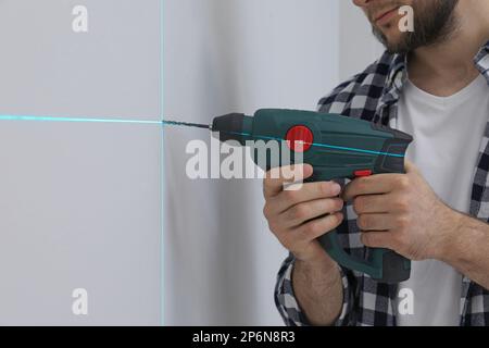 Man using cross line laser level for accurate measurement and drilling hole in light wall, closeup Stock Photo