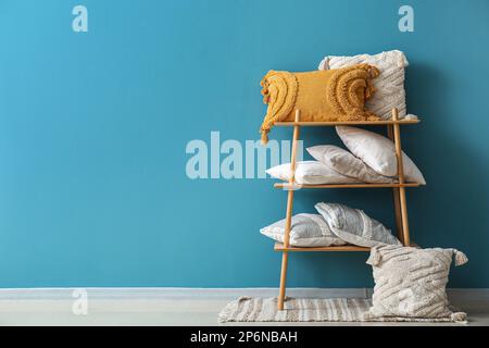 Stylish decorative pillows on shelving unit near blue wall Stock Photo