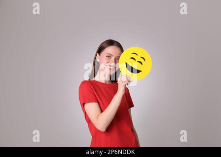 Happy young woman with laughing emoji on grey background Stock Photo