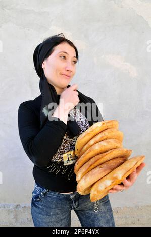 An Uzbek woman carrying local bread. Obi Non- is a traditional Uzbek / Tajik bread sold at the markets throughout Uzbekistan. Stock Photo