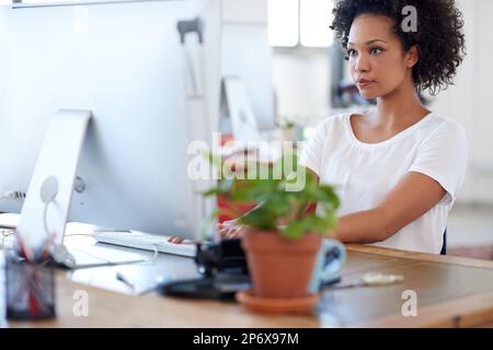 Shes doing business her way. Beautiful african businesswoman working on her pc at her desk in a bright office space. Stock Photo